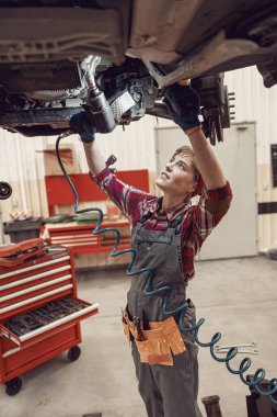 Serious woman standing under the lifted vehicle clipart