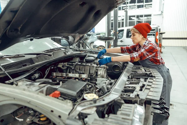 Geconcentreerde vrouwelijke monteur die een motorvoertuig inspecteert — Stockfoto