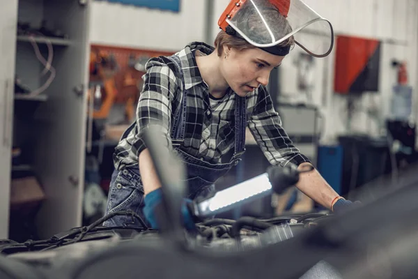 Ung kvinnlig mekaniker kontrollerar ett bilbatteri — Stockfoto