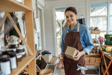 Siyah saçlı kız, elinde bir karton kutuyla ileriye bakıyor.