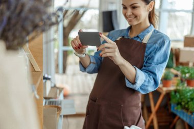 Gülümseyen çiçekçi bir dükkanda iş yerinin fotoğrafını çekiyor.
