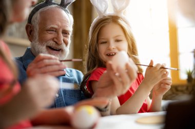 Excited grandfather and granddaughter painting eggs stock photo clipart