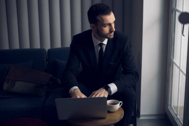 Kahve molası sırasında laptopun başında çalışan beyaz bir genç.