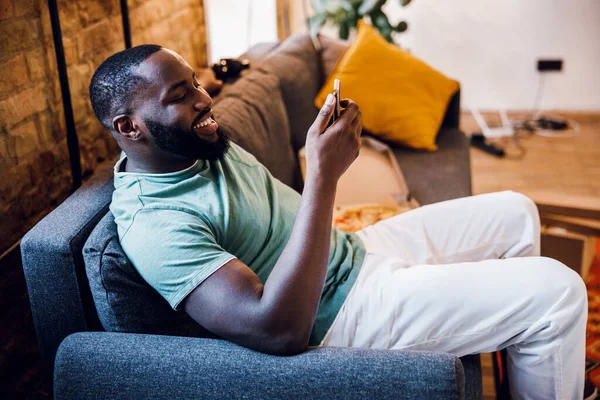 Gladjagende man met smartphone op de sofa stock foto — Stockfoto