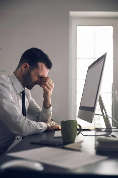 Homem caucasiano barbudo com dor de cabeça trabalhando no laptop no escritório — Fotografia de Stock