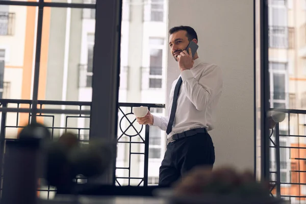 Красивый бизнесмен разговаривает по мобильному телефону возле балкона — стоковое фото