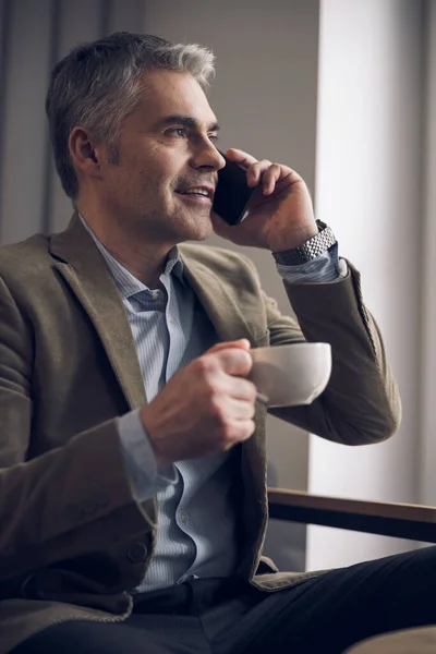 Caucasian satisfied businessman talking on smartphone during coffee break — Stock Photo, Image