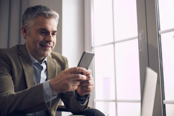 Caucasian smiling businessman using his mobile phone in office — Stock Photo, Image