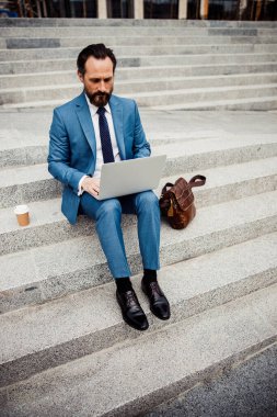 Modern erkek girişimci bilgisayarını açık havada kullanıyor.