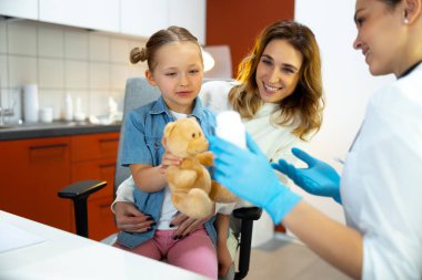 Hastanede, doktorun yanında annesinin dizlerinin üstünde oturan küçük çocuk.