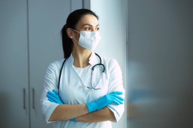 Pencereden bakan maskeli kadın doktor