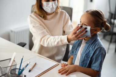Sorumlu anne klinikte kızının yüzüne tıbbi maske takıyor.