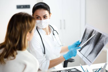 Omurganın röntgen fotoğrafını saklayan tıbbi maskeli hoş bir çocuk doktoru.