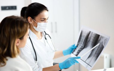 Steteskoplu zeki bir çocuk doktoru annesiyle omurga röntgenini tartışıyor.