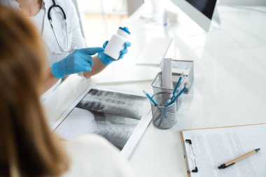 Lastik eldivenli çocuk doktorunun hastaya ilaç şişesini gösterirken çekilmiş fotoğrafı.
