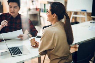 Güzel bayan dizüstü bilgisayarla masada oturuyor ve iş arkadaşına bakıyor.
