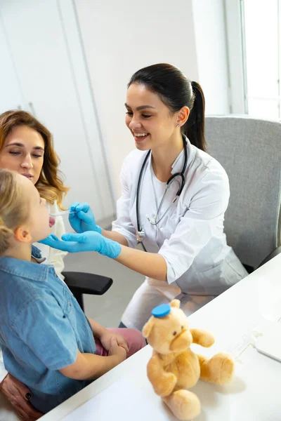 Schöne Ärztin in Gummihandschuhen schaut kleine Patientin an — Stockfoto