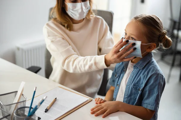 Responsible mum putting medical mask on face of her daughter in clinic