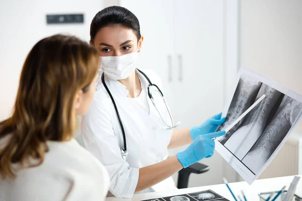 Calma bastante pediatra en máscara médica mantenimiento de rayos X foto de la columna vertebral — Foto de Stock