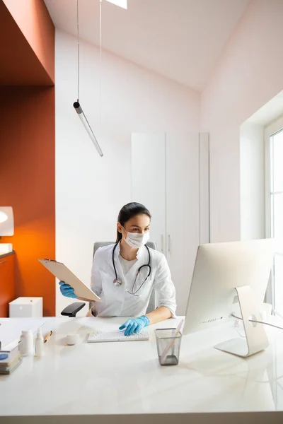 Caucasian doctor in medical mask typing results of examination in database