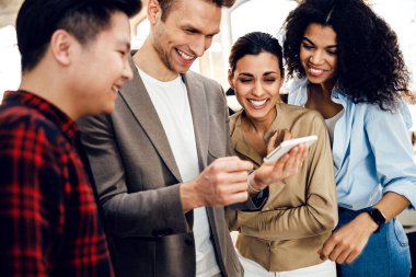 Neşeli çok ırklı insanlar cep telefonundan komik videolar izliyorlar.