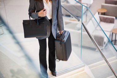 Bavullu bayan, kalkış salonundaki merdivenlerin üstünde duruyor.