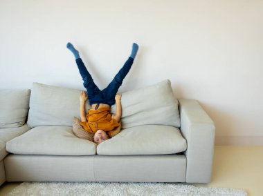 Sevimli küçük çocuk kanepede başının üstünde duruyor