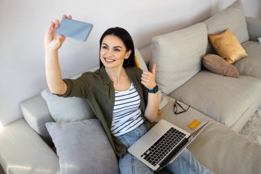 Çekici genç bir kadın selfie çekiyor ve baş parmağını kaldırıyor.