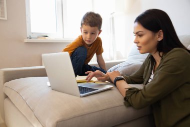 Cute little boy and his mother using laptop at home clipart
