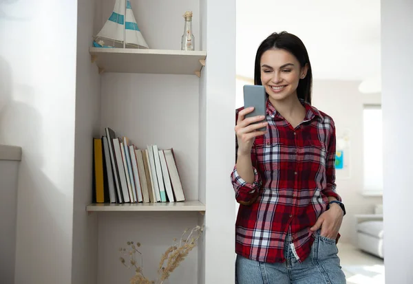 Merry young woman using smart phone indoors