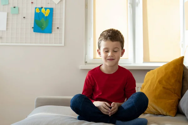 Smiling boy meditating on couch at home — Stock Photo, Image