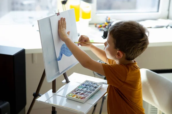 Симпатичный маленький мальчик рисует картину на мольберте — стоковое фото