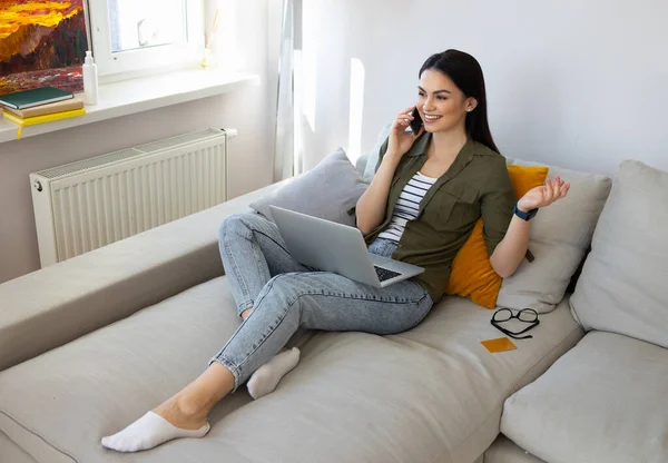 Vacker dam som använder laptop och pratar på mobiltelefon hemma — Stockfoto