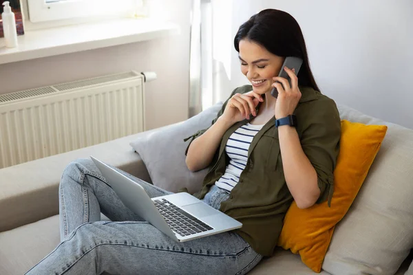 Glada söt dam som använder laptop och har telefon konversation — Stockfoto