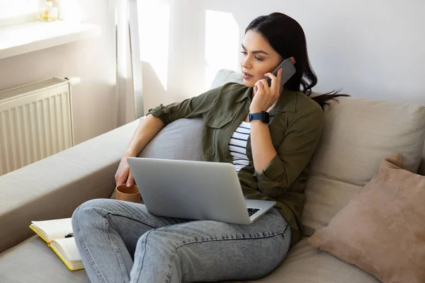 Gyönyörű fiatal nő használja laptop és beszél a mobiltelefon otthon — Stock Fotó