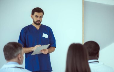 Yakışıklı doktor iş arkadaşlarıyla toplantı sırasında not alıyor.