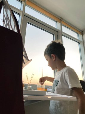 Evdeki pencerenin yanında resim yapan sevimli çocuk.