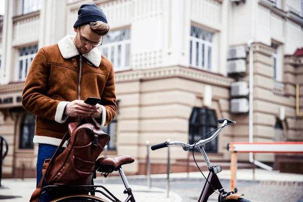 Спокойный человек со смартфоном и велосипедом на фото города — стоковое фото