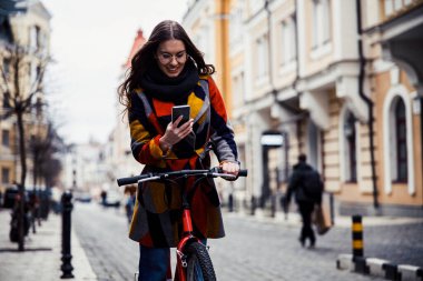 Bisiklet sürerken akıllı telefona bakan memnun bir bayan.