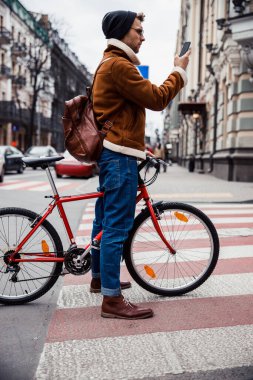 Yaya geçidinde akıllı telefonla duran ciddi bir bisikletçi.