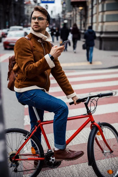 Bedachtzame jonge fietser met smartphone op zoek weg stock foto — Stockfoto