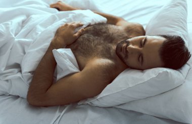 Mutlu ve çekici bir adam rahat bir yatakta uyuyor.