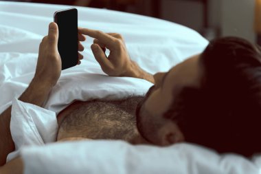 Genç adam yatakta akıllı telefon kullanıyor.