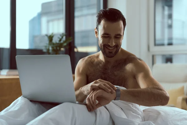 Hombre feliz con cuaderno mirando el reloj en la cama — Foto de Stock