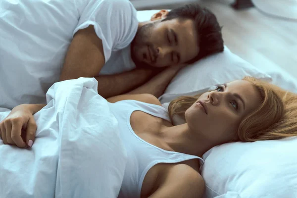 Молодая красивая женщина просыпается рядом со спящим мужчиной — стоковое фото
