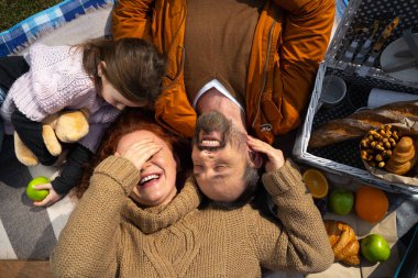 Sevgi dolu ebeveynler kızlarıyla battaniyeye uzanıp gülüyorlar.