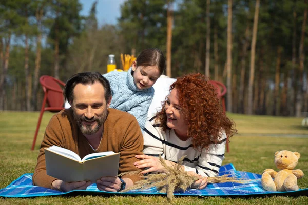 Улыбающийся мужчина читает книгу своей милой дочери и жене — стоковое фото