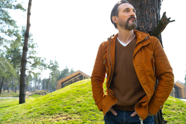 Handsome bearded man standing near tree and looking away