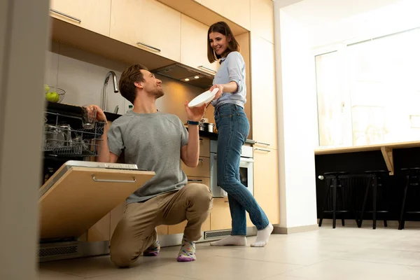 A férj mosogatógépbe teszi az edényeket otthon. — Stock Fotó
