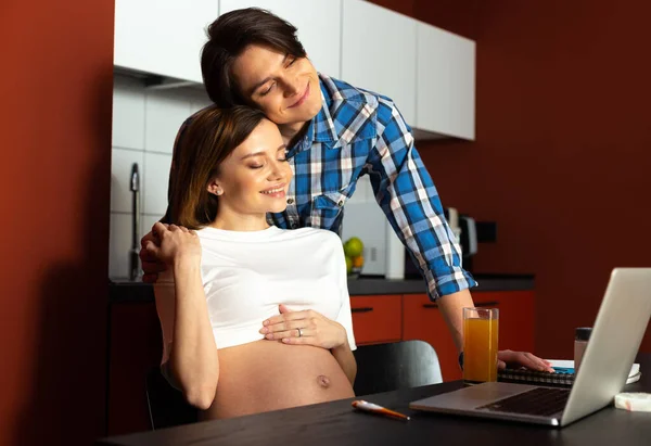 Lächelndes Paar umarmt sich in der Küche, während es ein Baby erwartet — Stockfoto